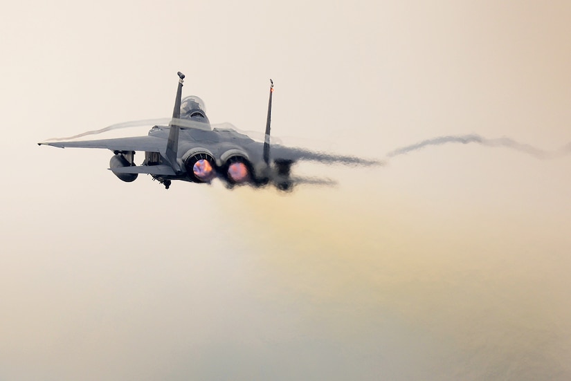 A twin-engine military fighter jet flies through a hazy sky.