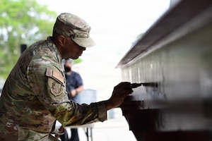 A man in military uniform signs a steel beam.