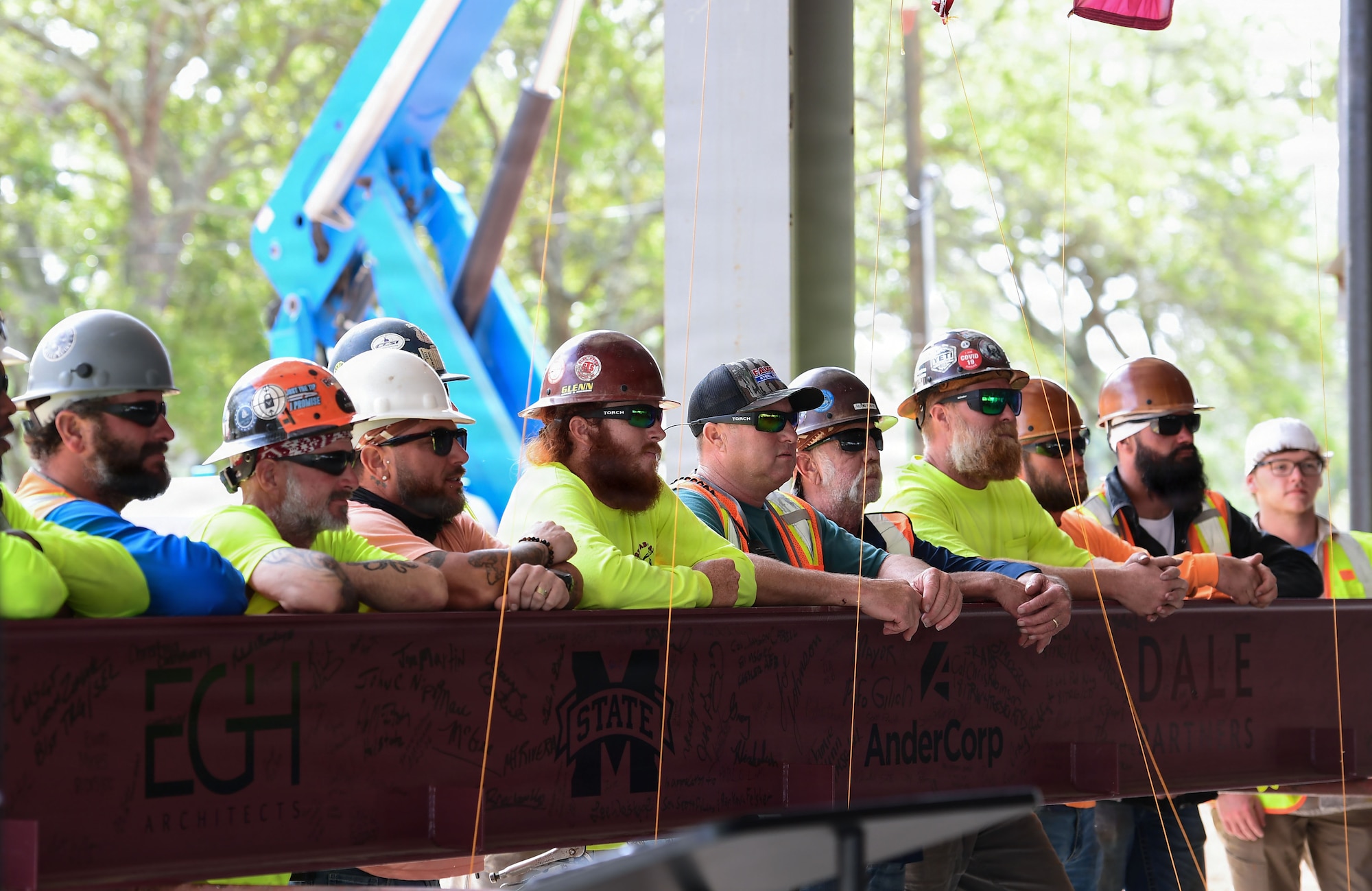 Construction workers stand behind a steel beam for a photo.