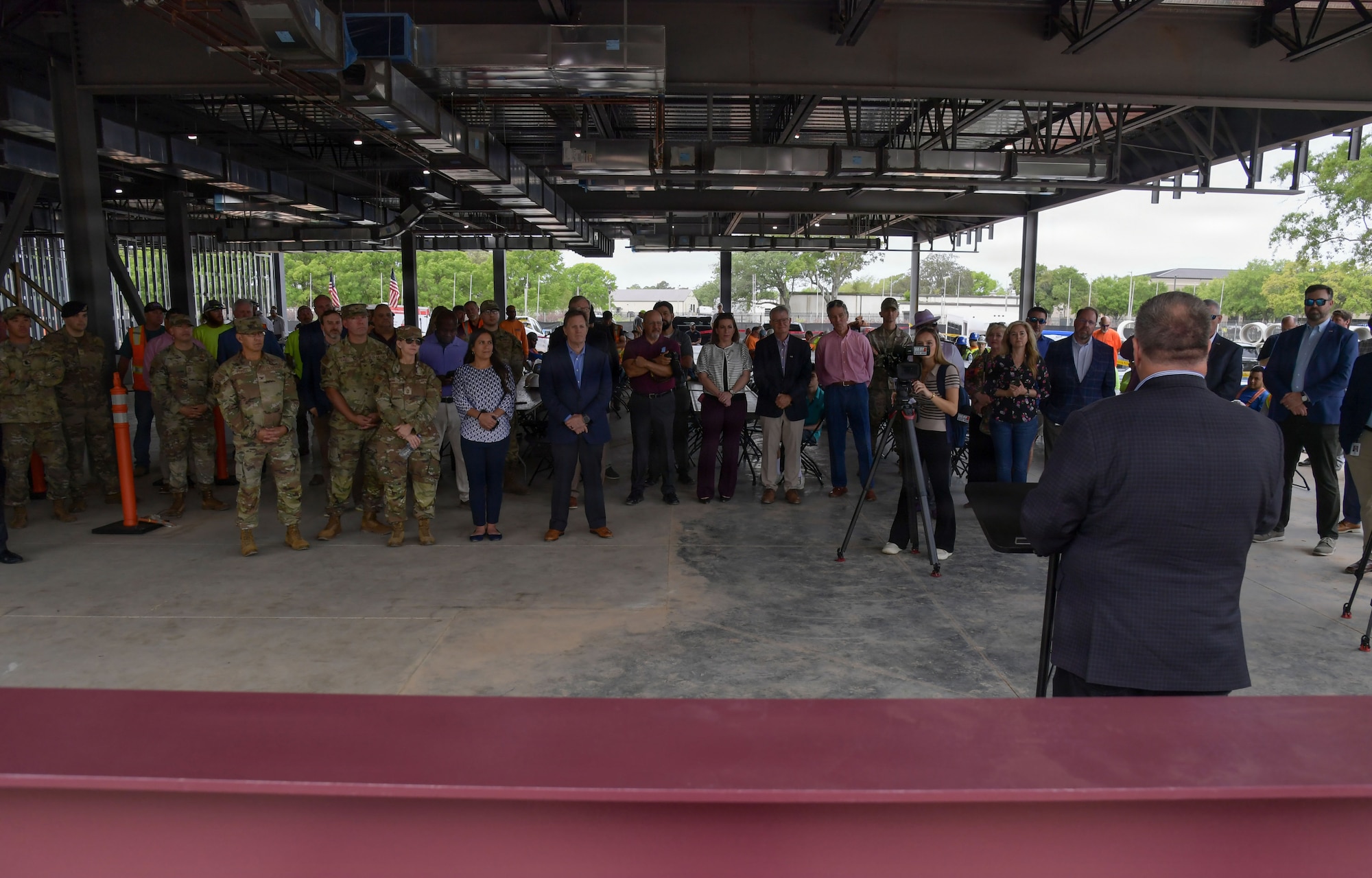 A man speaks to a crowd of people inside a building structure.