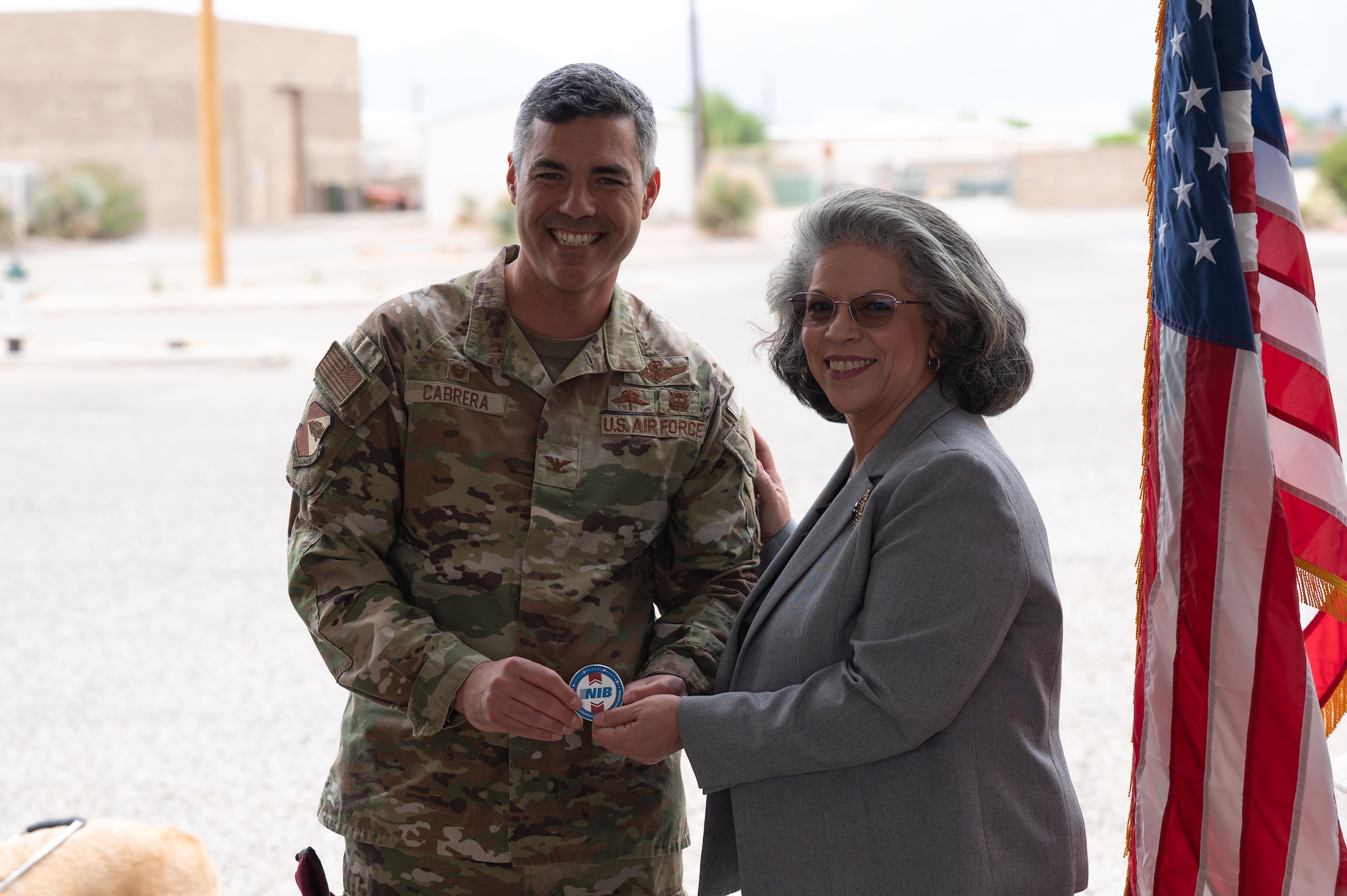 Soraya Correa, National Industries for the Blind president, right, presents U.S. Air Force Col. Jose Cabrera, 355th Wing commander, left, a coin of recognition during the AbilityOne Base Supply Center 30th Anniversary Ceremony at Davis-Monthan Air Force Base, Arizona, April 6, 2026. The coining recognized Cabrera’s support of the AbilityOne Program and its mission to create employment opportunities for individuals with disabilities. (U.S. Air Force photo by Airman 1st Class Jaden Kidd)
