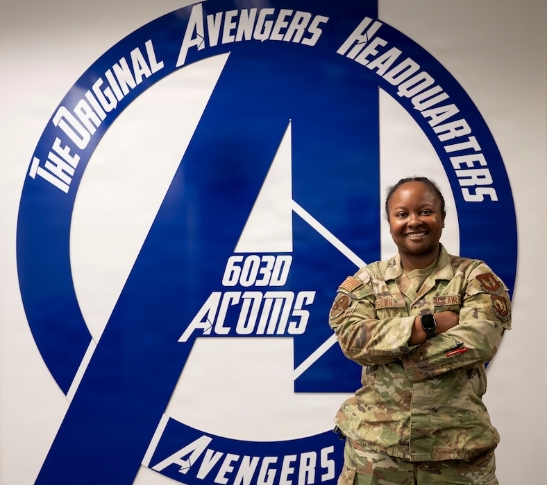 U.S. Air Force Staff Sgt. Briona Brown, 603rd Air Communications Squadron noncommissioned officer in charge of the Global Command and Control Systems, poses for a photo in front of a blue and white 603D ACOMS sign at Ramstein Air Base, Germany. She takes care of Airmen who support the mission of securing communication and cyber capabilities, enabling safe and fluid operations across the base. (U.S. Air Force photo by Airman 1st Class Joseph Curzi)