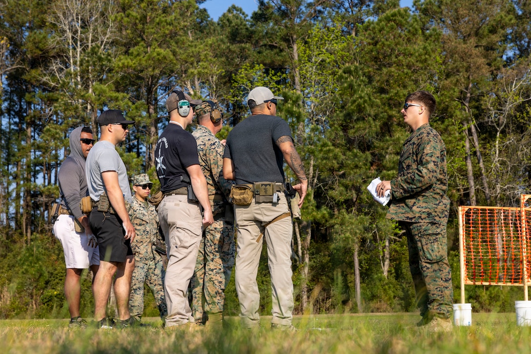 A U.S. Marine Corps combat marksmanship coach, right, briefs Marines and Sailors with 2nd Marine Logistics Group before commencing the next stage of an Action Shooting Program competition at Marine Corps Base Camp Lejeune, North Carolina, March 27, 2026. The ASP hosts community events for Marines, Sailors, and civilians alike to build camaraderie and test individual shooting skills. The event is part of the Marine Corps Competition in Arms Program and serves as an endorsement for competitive marksmanship for Marines and Sailors within Marine Corps Installation East, MCB Camp Lejeune. (U.S. Marine Corps photo by Lance Cpl. Isabella Ramos)