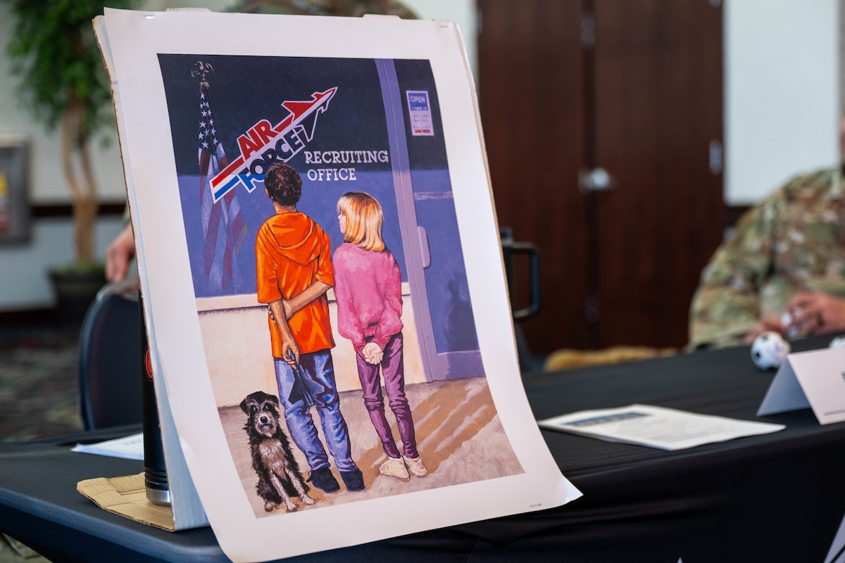 A sign is displayed of 2 children and a dog. The dog sits on the left, looking towards towards you, with a boy in the center looking away, at a glass that says "Air Force." There is a girl on the right, who is looking up to the boy.