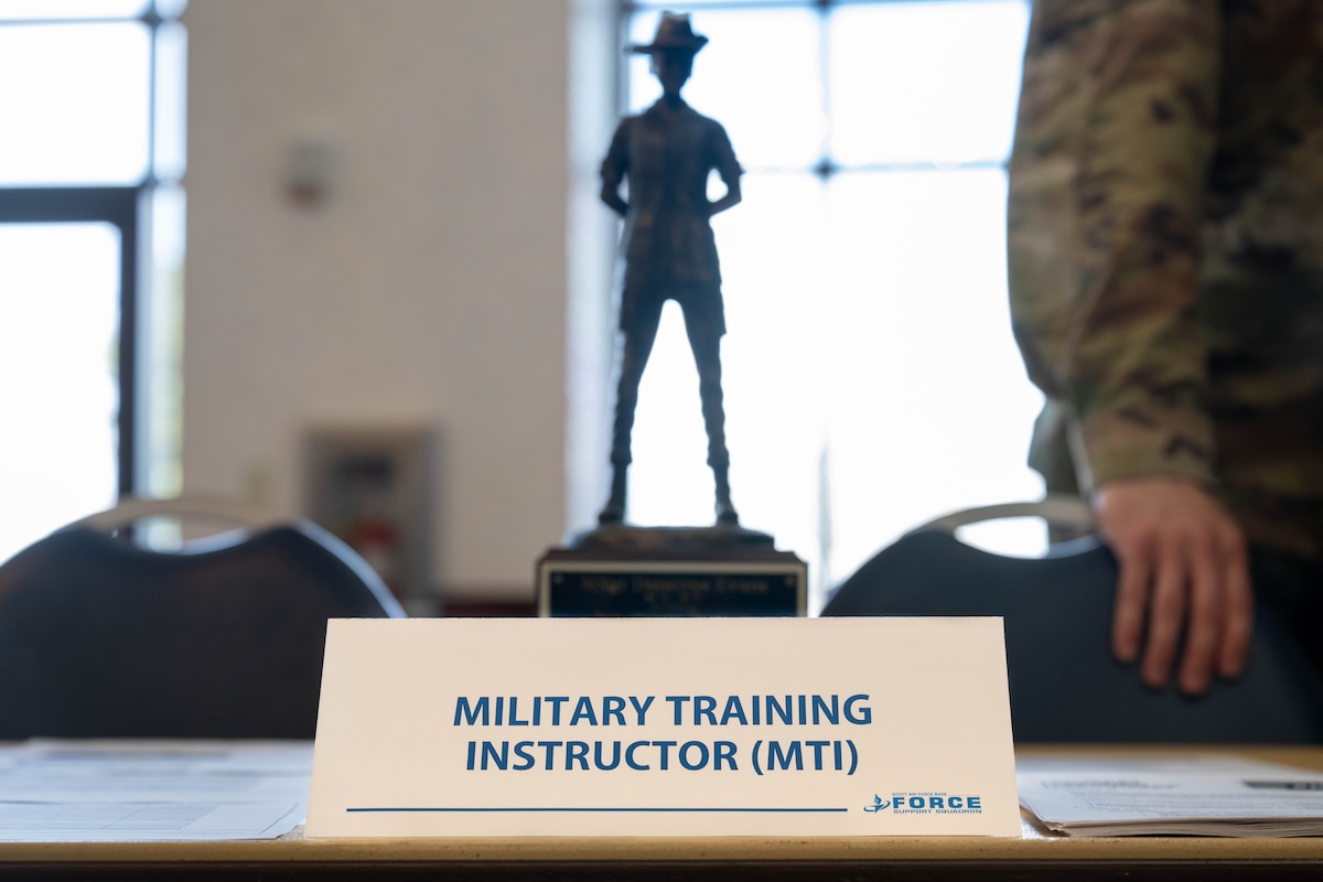 A name card is displayed, with the words "Military Training Instructor (MTI)." A statue stands behind the card, of a woman with her hands behind her back, and an MTI hat on.