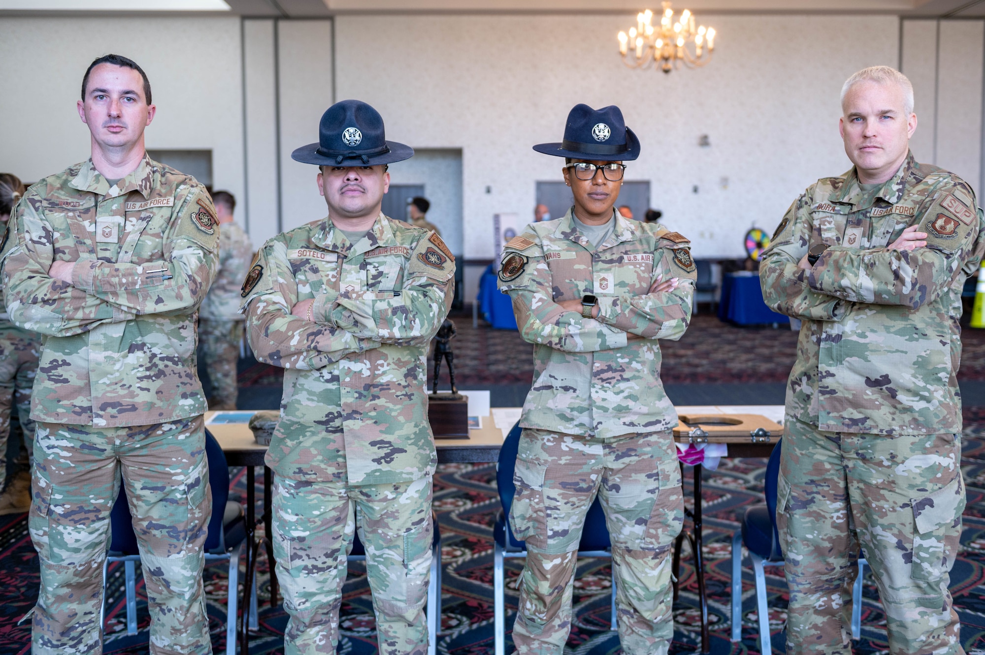 4 Airmen with their arms cross. The gentleman in the center left and lady in the center right have a military training instructor hat on.