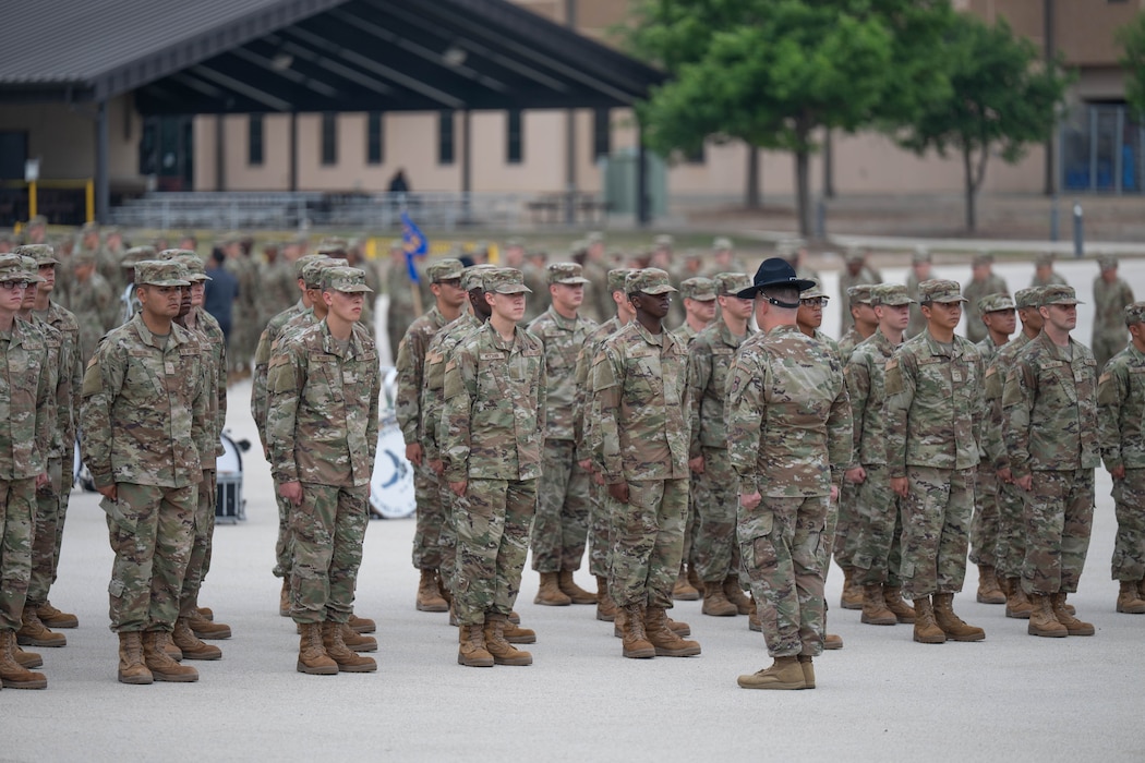 U.S. Air Force Basic Military Training trainees stand at attention in front of a military training instructor (MTI) during the Coin and Retreat Ceremony at Joint Base San Antonio-Lackland, Texas, April 1, 2026. MTIs are responsible for teaching trainees discipline, bearing and core values during Basic Military Training. (U.S. Air Force photo by Airman 1st Class Emma Wright)
