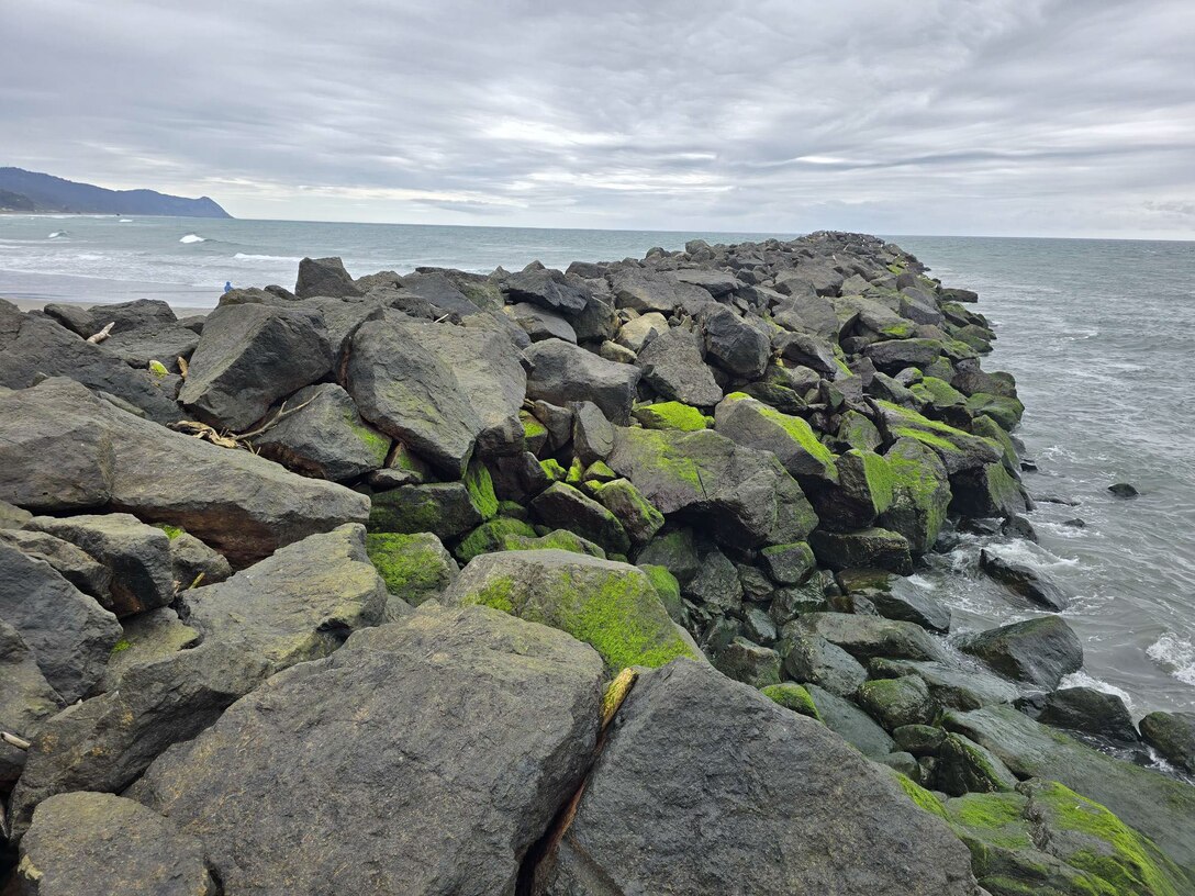 large stones, some moss covered, create the Rogue River South Jetty that extends out into the horizon of the Pacific Ocean
