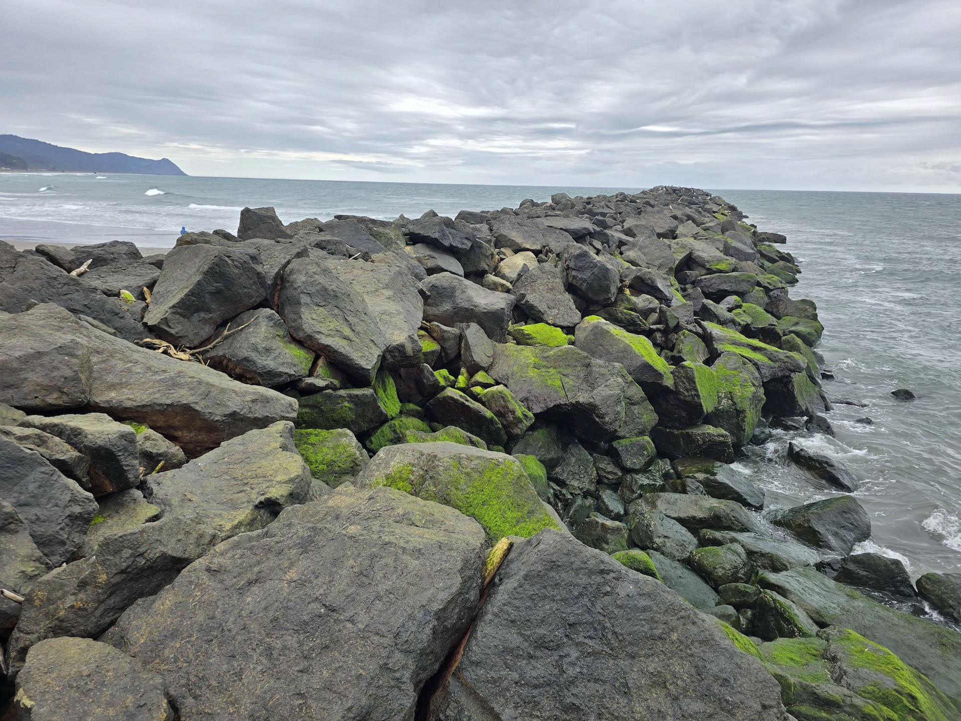 large stones, some moss covered, create the Rogue River South Jetty that extends out into the horizon of the Pacific Ocean