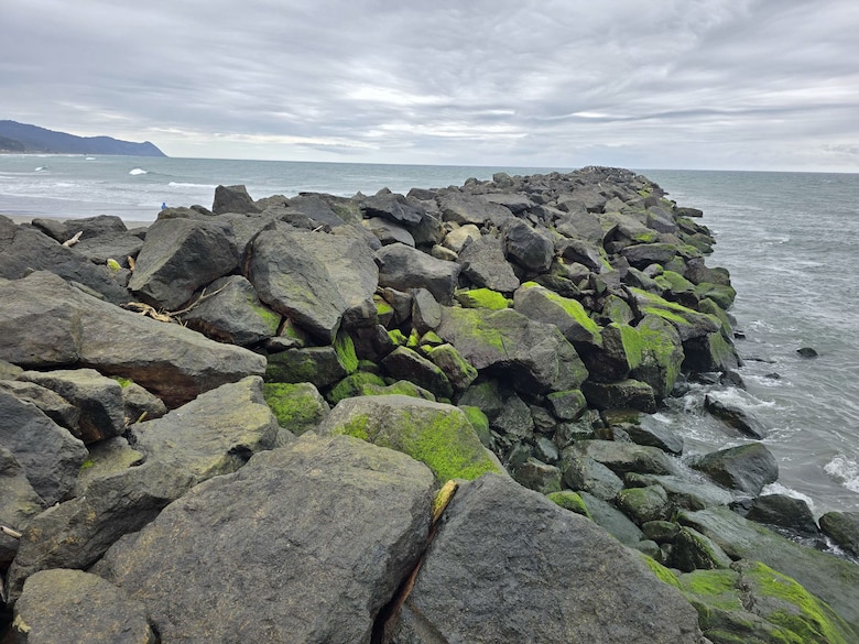 large stones, some moss covered, create the Rogue River South Jetty that extends out into the horizon of the Pacific Ocean