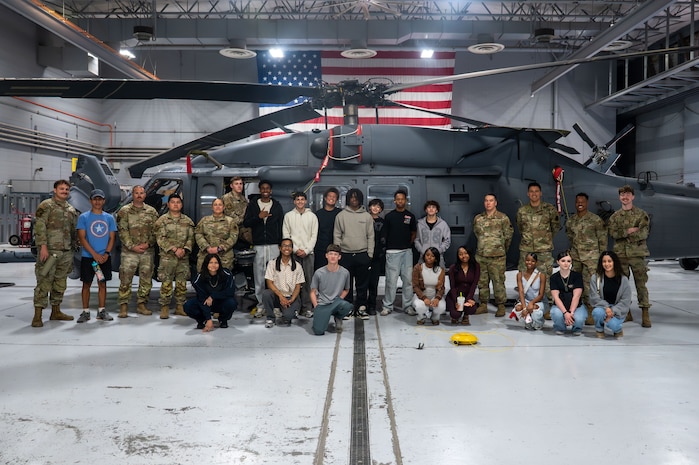 Airmen pose with foster teens in front of military helicopter