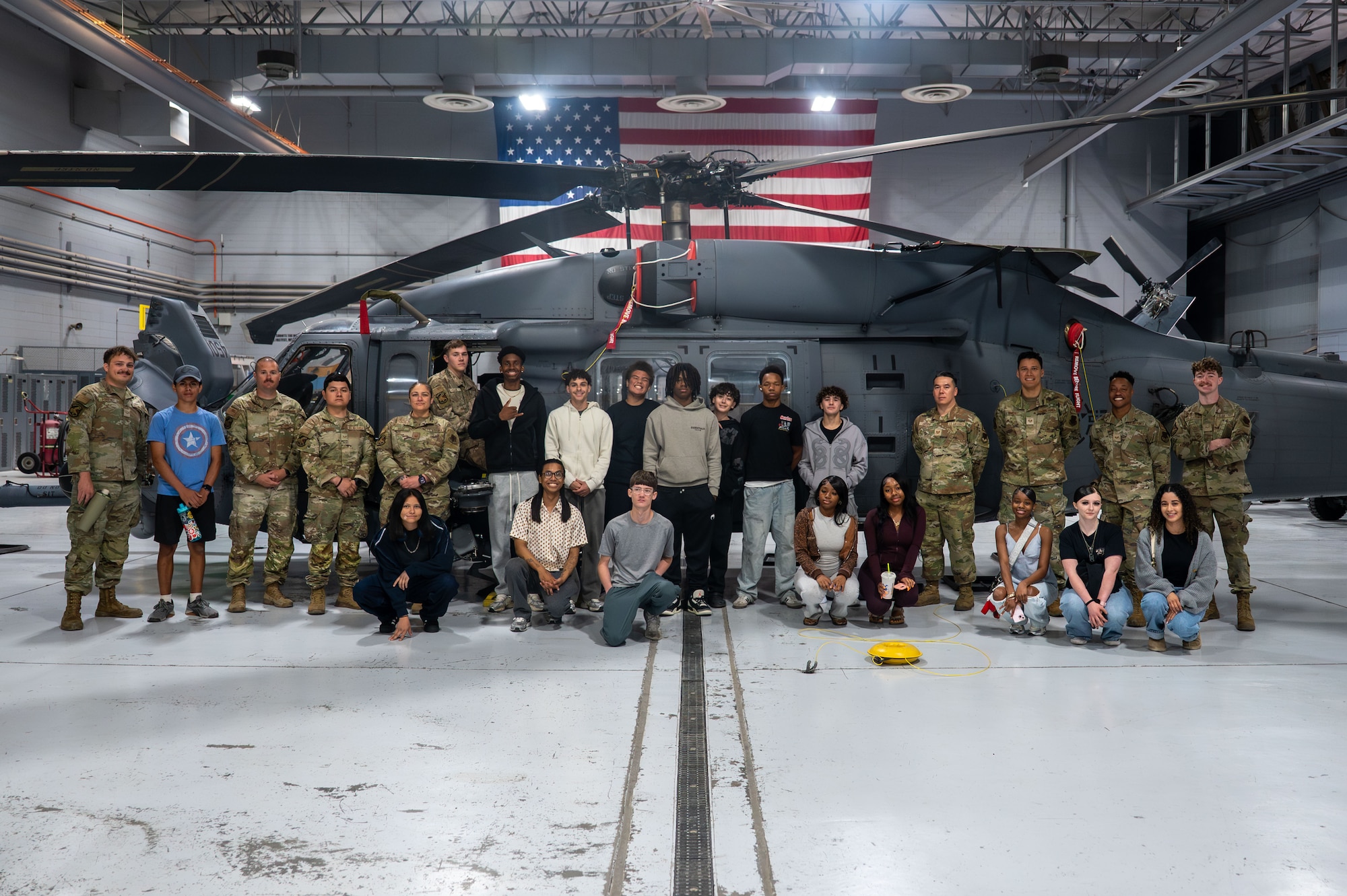 Airmen pose with foster teens in front of military helicopter