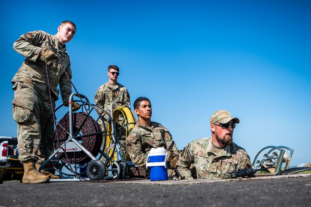 A group of people pull a cable through a tunnel in the ground.