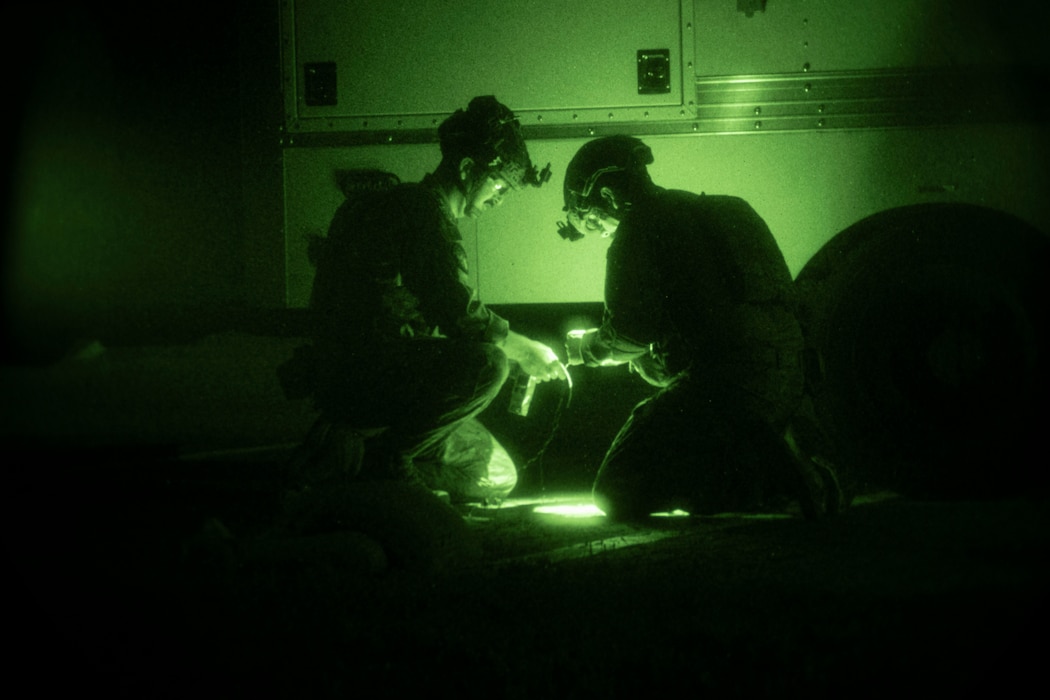 Two people crouch over an electronic device at night.