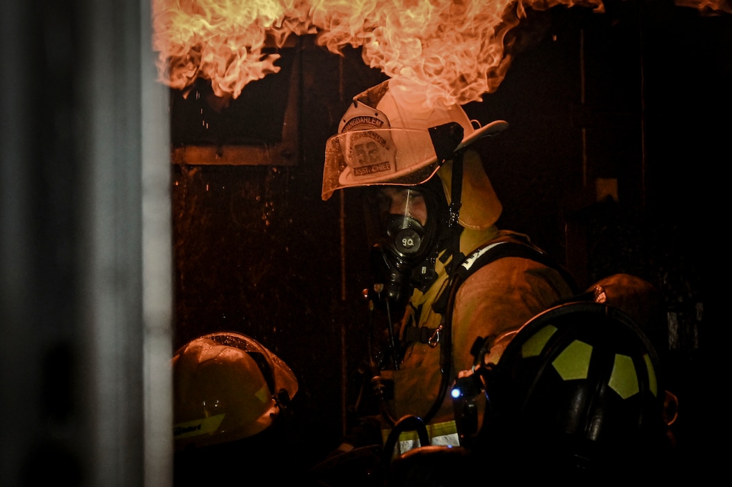 A firefighter wearing a protective suit stands in flames.