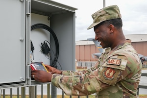 an Airman smiles while holding a red Wet Bulb Globe Temperature meter
