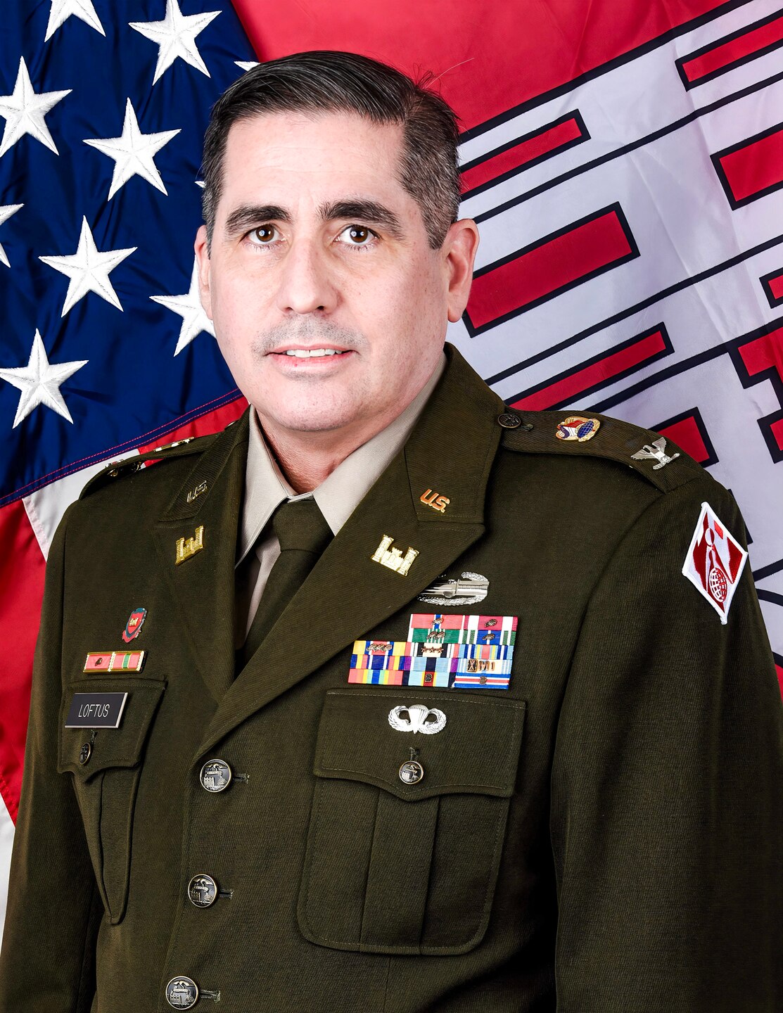 An Army officer in dress uniform poses for an official photo in front of the U.S. and U.S. Army Corps of Engineers flags