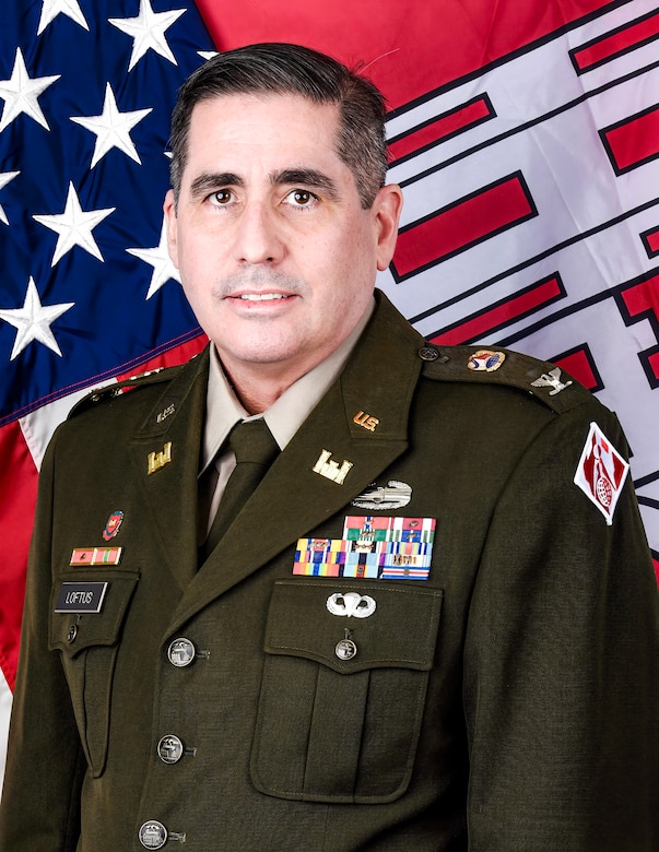 An Army officer in dress uniform poses for an official photo in front of the U.S. and U.S. Army Corps of Engineers flags