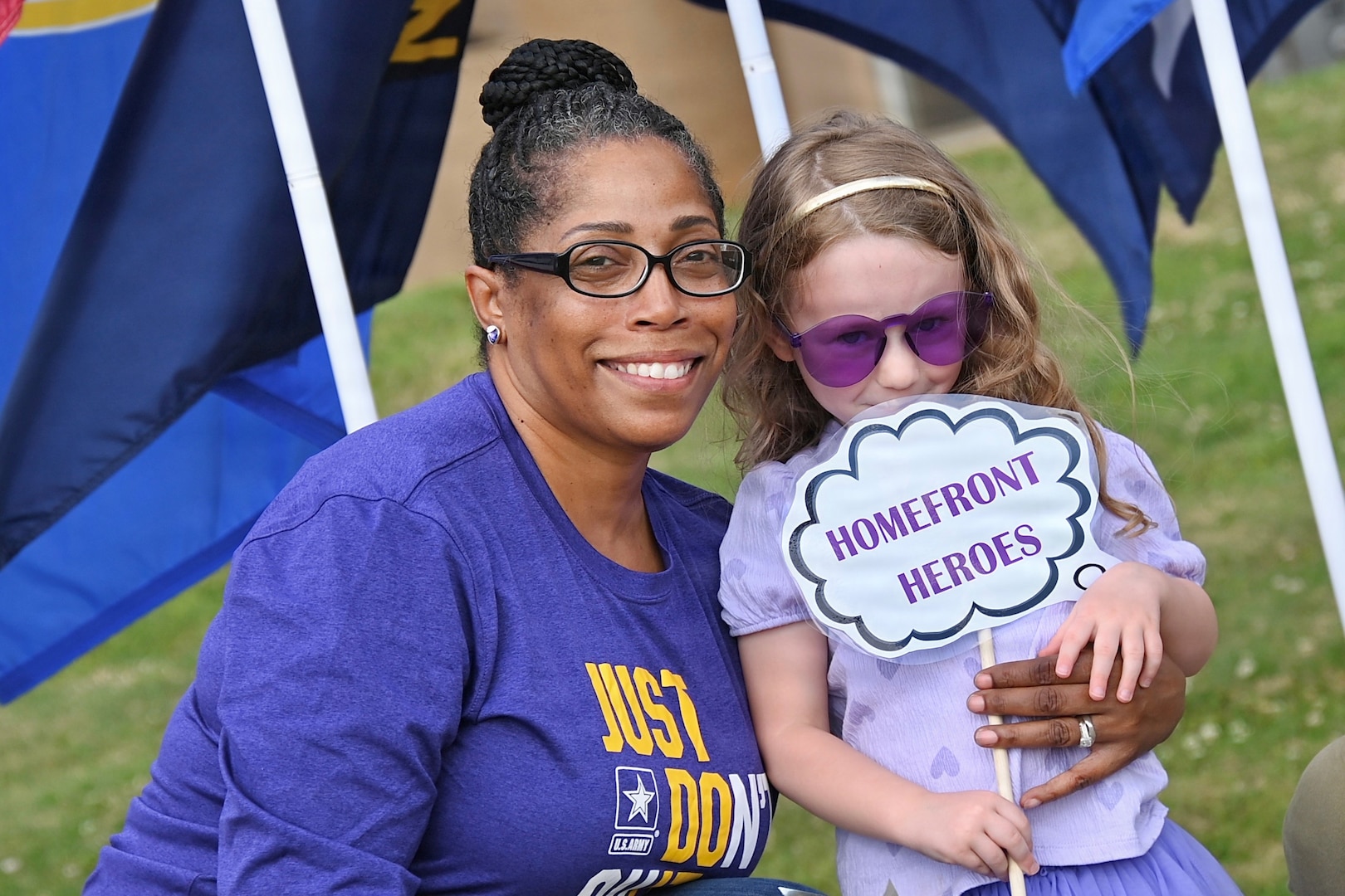 Mother poses with her daughter who holds a "Homefront Heroes" sign.