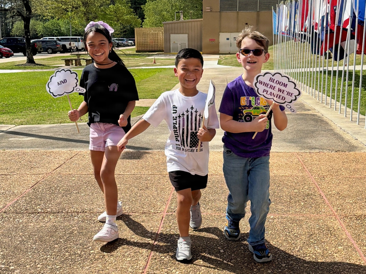 Three kids carrying hand signs walking in front of a line of flags.
