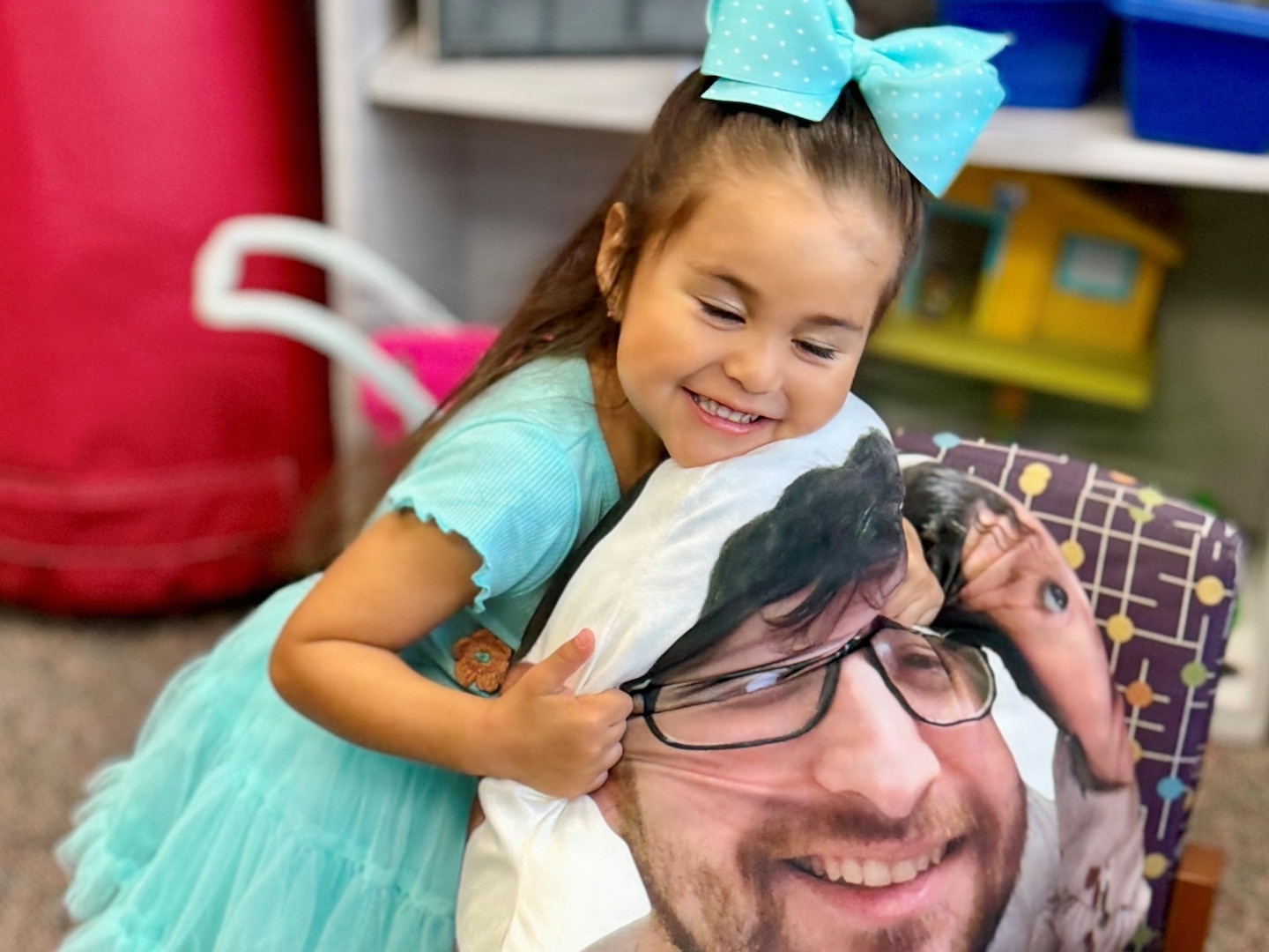 Girl hugging a pillow with her father's face printed on it.