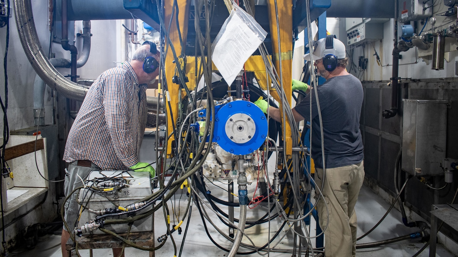 Anthony Jones, left, and Grady Mayo, artisans in the Fleet Readiness Center East Engine Driven Compressor and Gas Turbine Compressor Shop, connect a C-2A Greyhound auxiliary power unit to a test stand to check the component’s functionality.