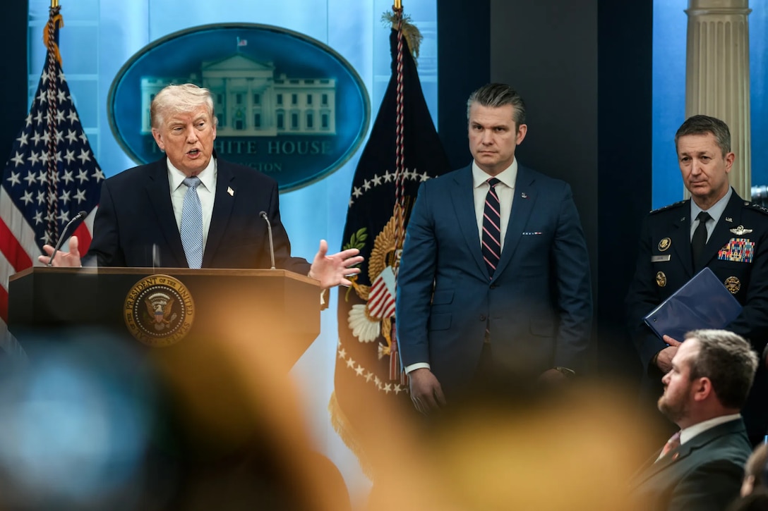 President Donald J. Trump speaks at a lectern as the secretary of war and chairman of the Joint Chiefs of Staff stand by.