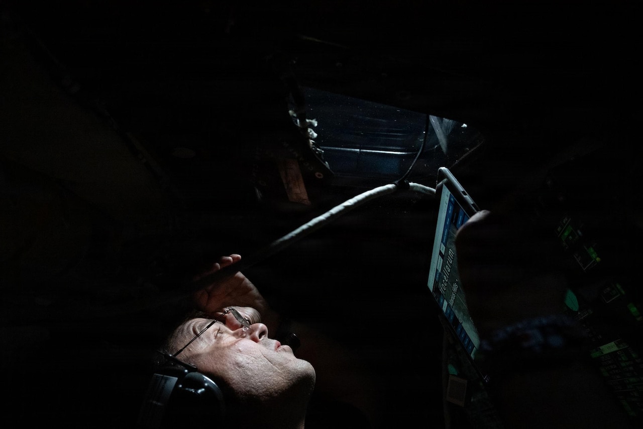 Light shines on a man's face as he looks out the window of a spacecraft.