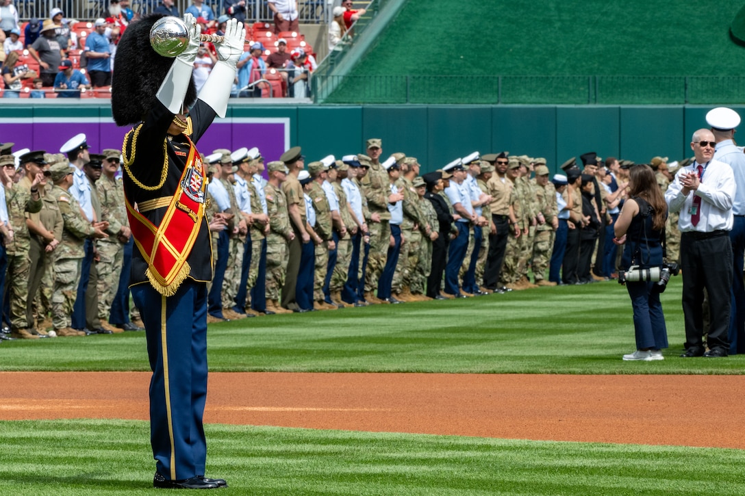 Service members hold U.S. flag on baseball field.