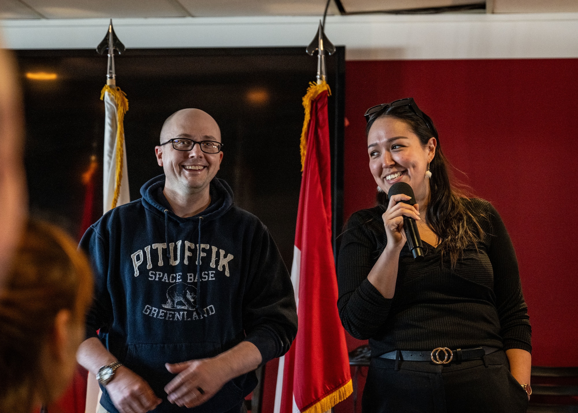 Two individuals stands in front of flags at award ceremony.