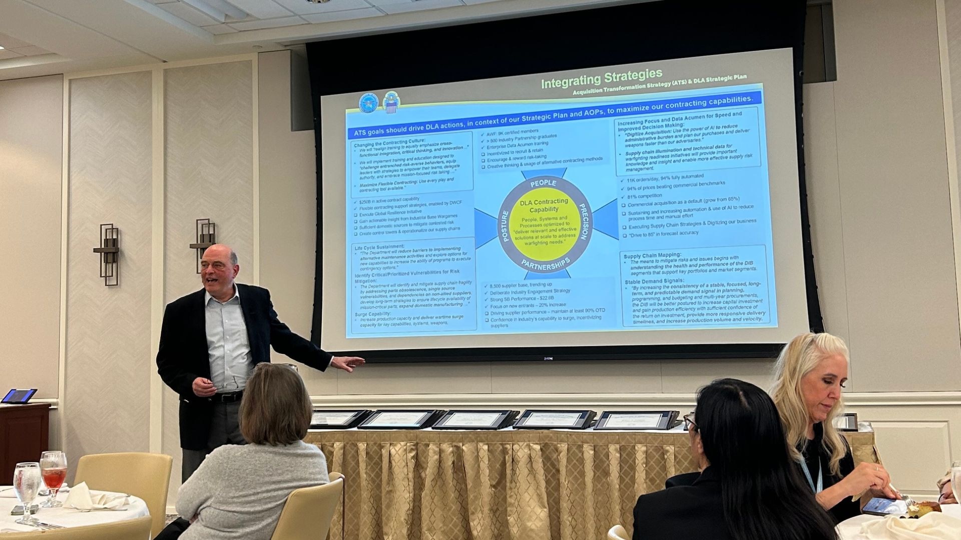 A man stands in front of a screen projection, pointing at the screen