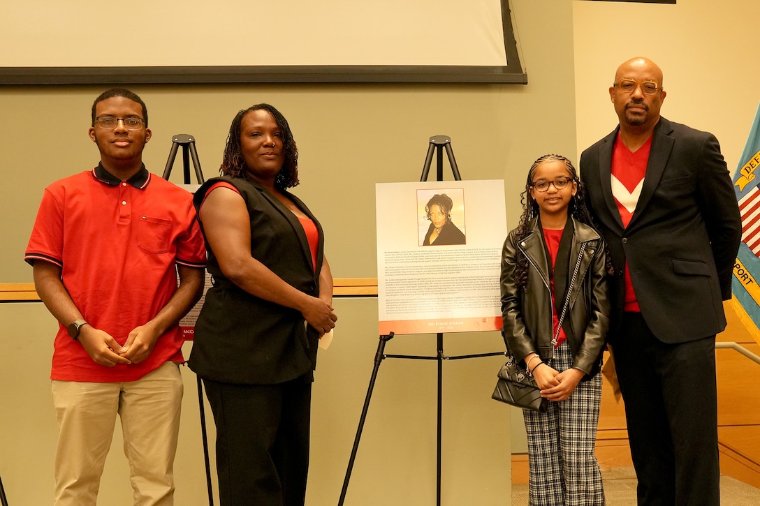 young man, left, woman, young girl and man, right, stand next to plaque on stage