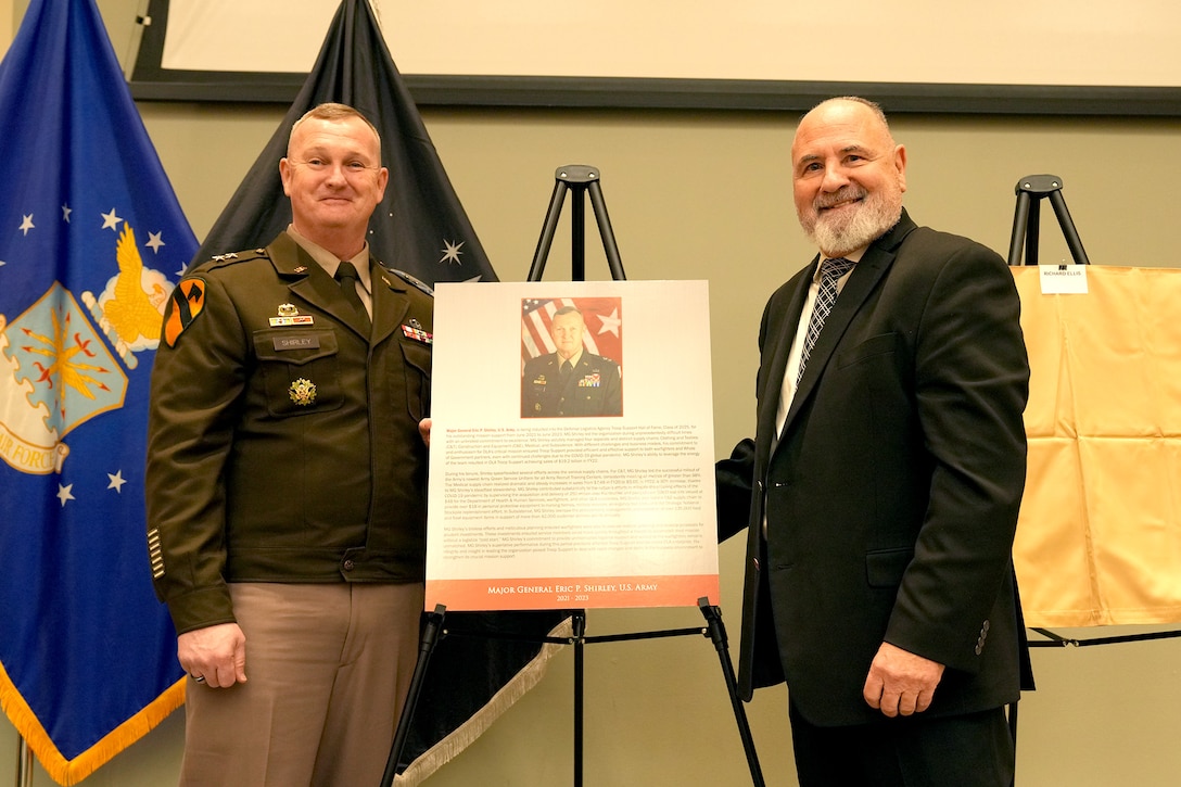 man in uniform stands left of plaque with man in suit