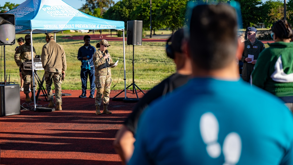 An Airman in the background in focus speaks while the audience in the foreground listens, backs to the viewer