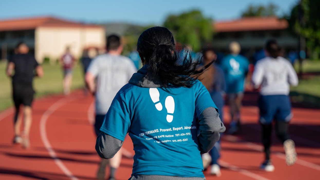 A shot from behind of an Airman wearing a SAAPM shirt running with other people out of focus ahead of her