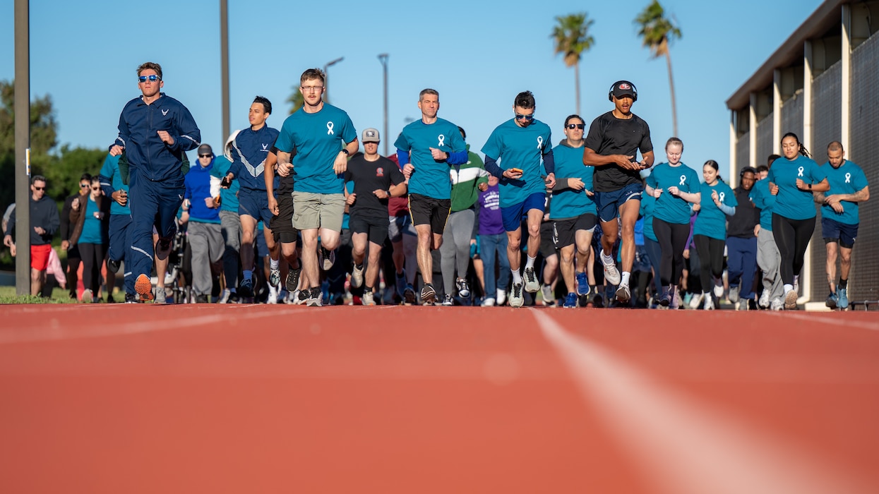 A large group of Airmen and civilians run on a track together