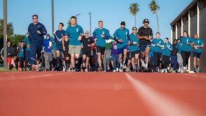 A large group of Airmen and civilians run on a track together
