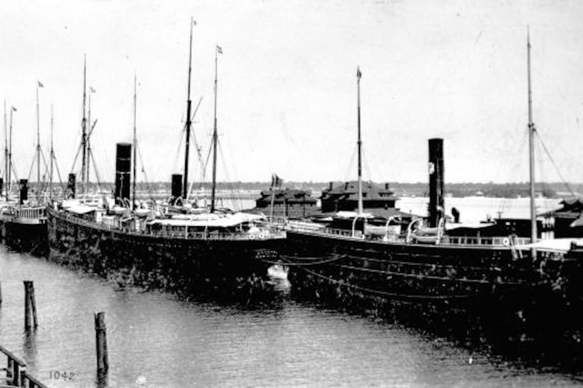 A black and white photo of several small steamships tied up in a port.