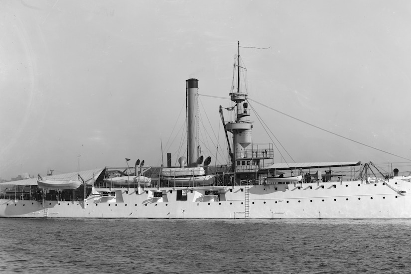 A black and white photo of a large gunboat docked in a harbor.