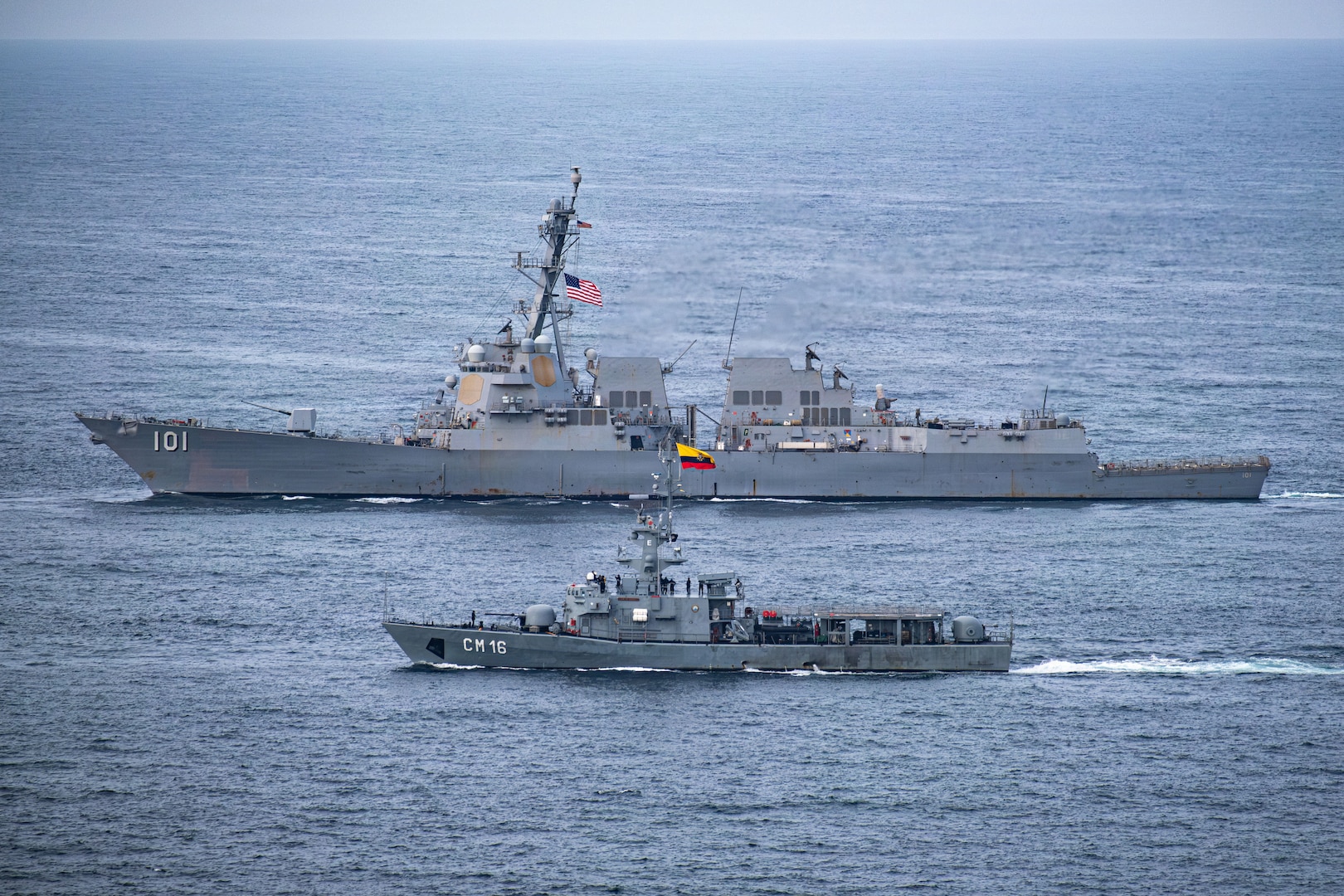 Two naval warships sail alongside each other.