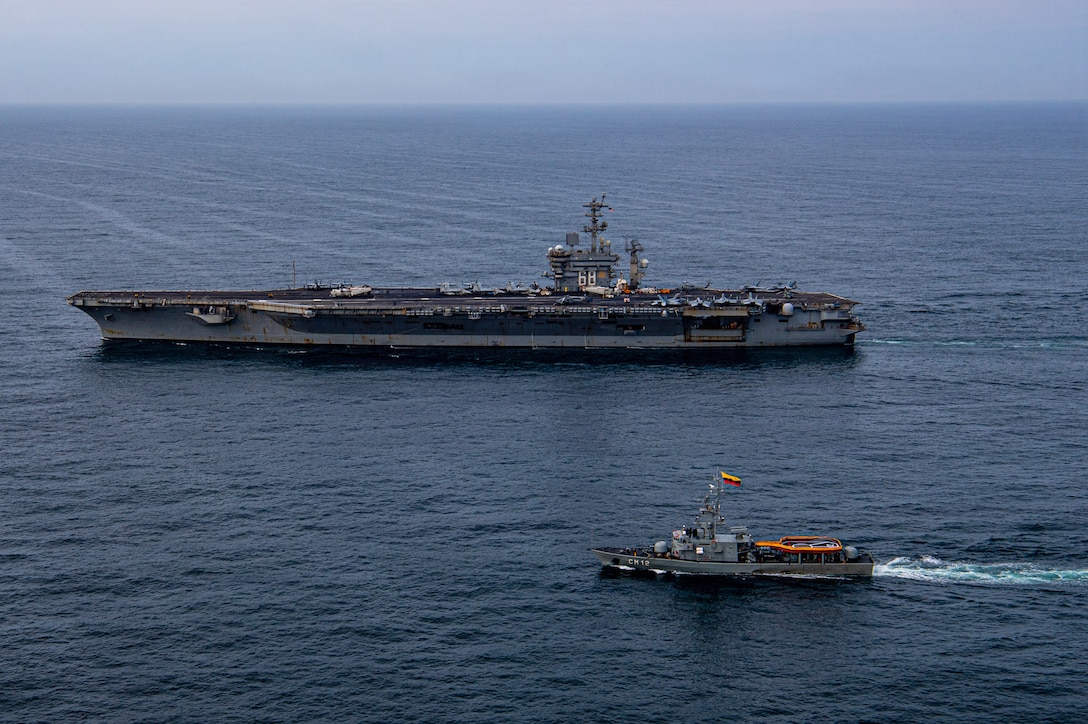 An aircraft carrier and a naval warship sail alongside each other.