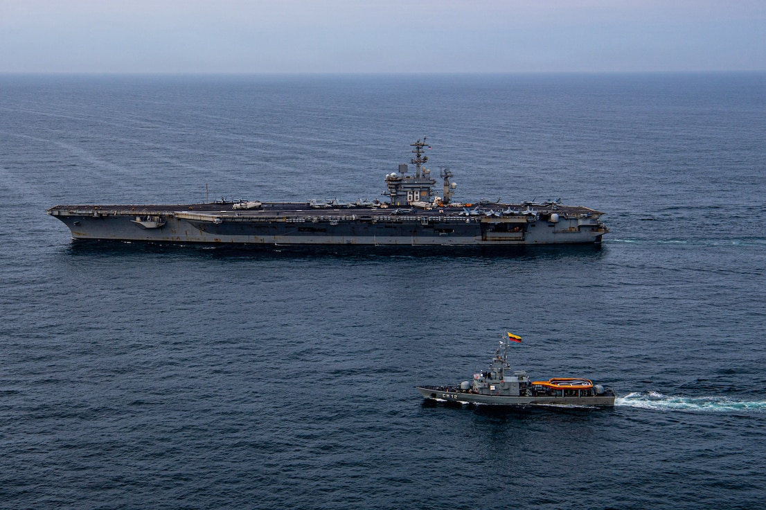 An aircraft carrier and a naval warship sail alongside each other.