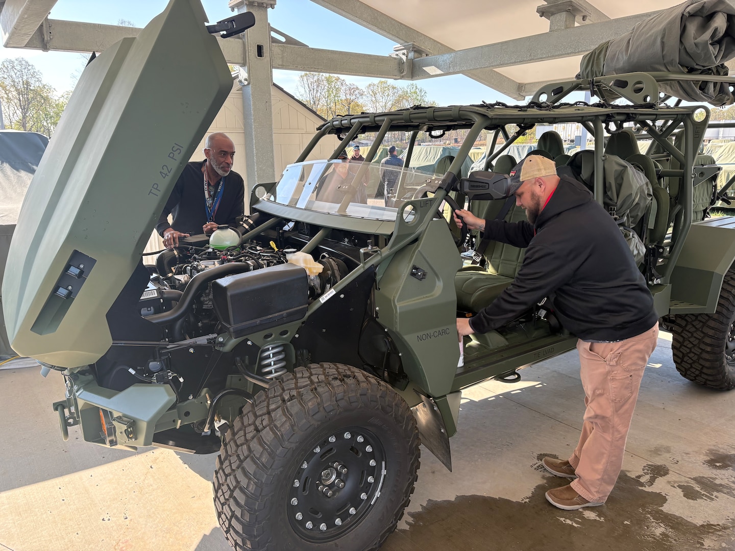 Two men look around a green military vehicle