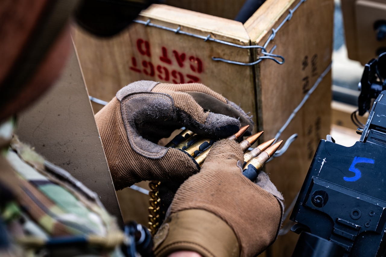 A person wearing a camouflage military uniform and tactical gear prepares ammunition for firing.