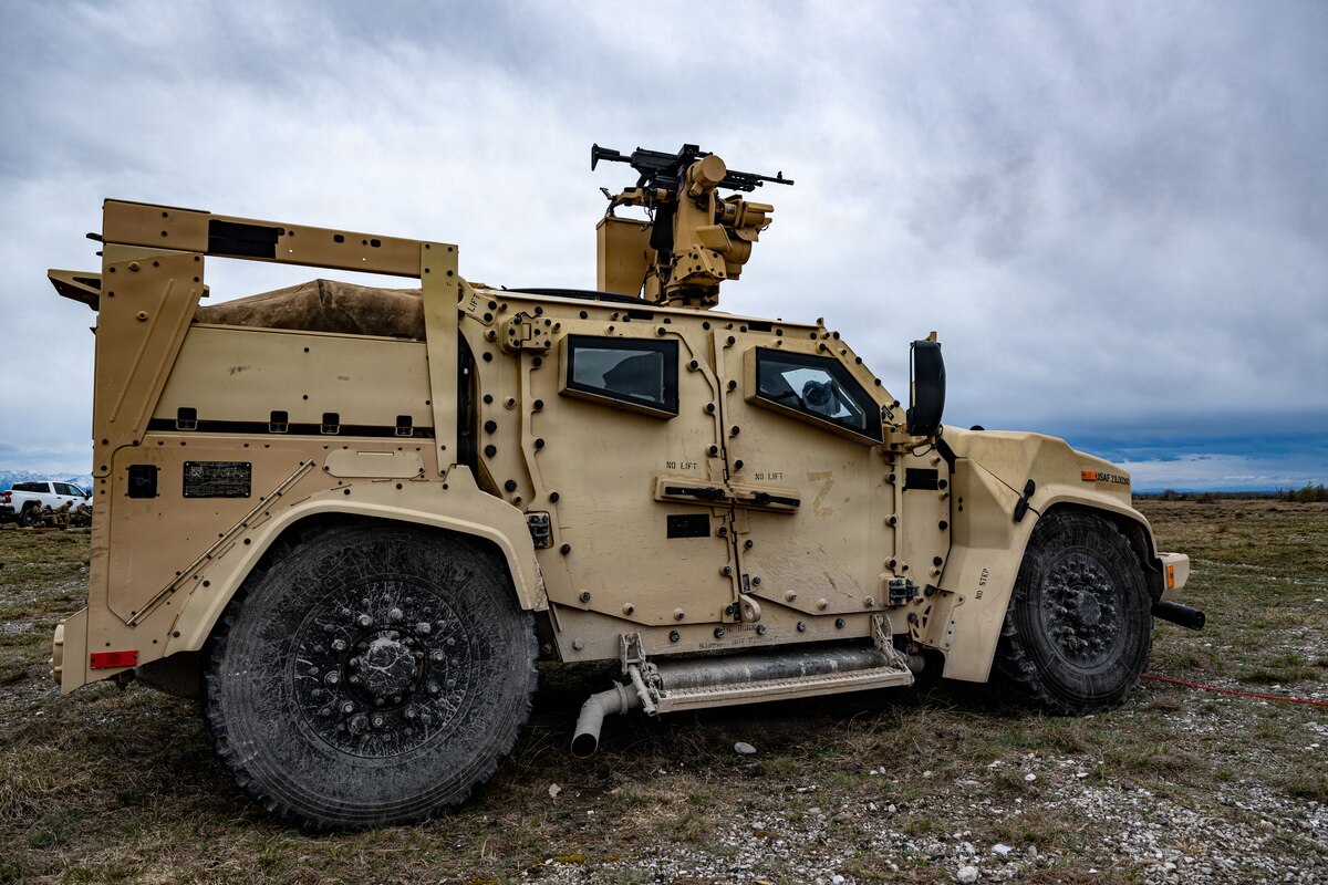 A military vehicle with a machine gun on top is parked near a seashore.
