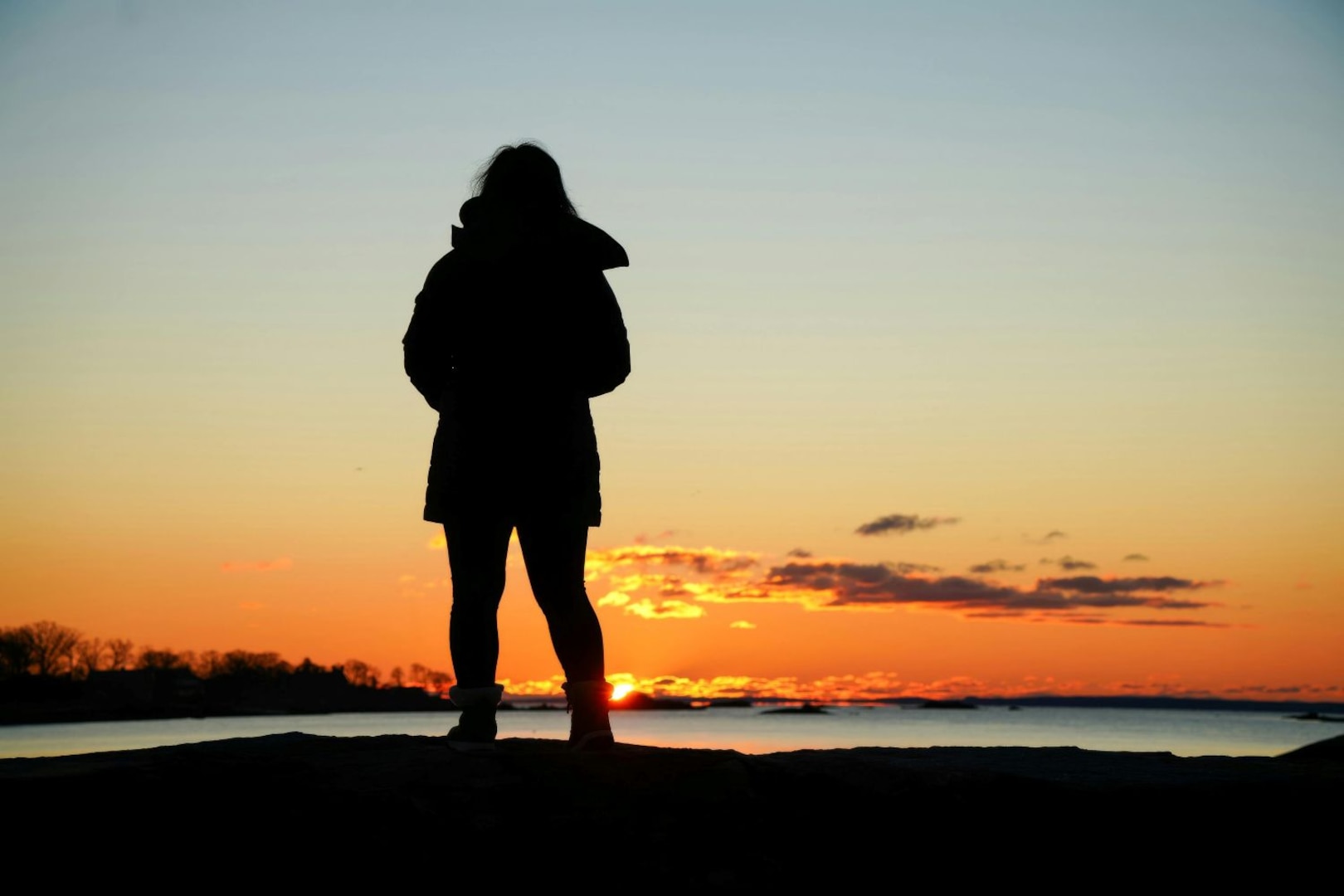 Silhouette of woman wearing coat standing on beach at sunset