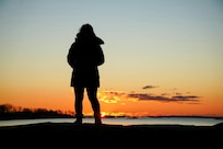 Silhouette of woman wearing coat standing on beach at sunset