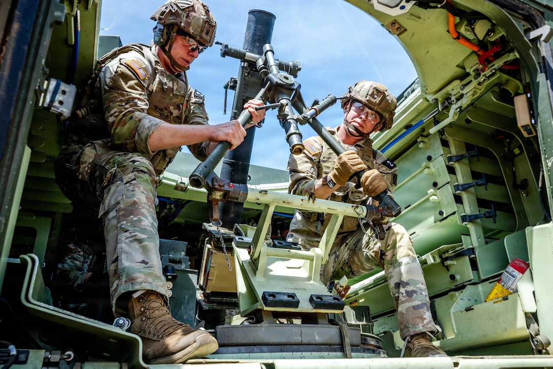 Soldiers in tactical gear use tools in a military vehicle under a blue sky.