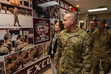 Chief Master Sergeant of the Air Force David R. Wolfe and his wife, Dr. Doniel Wolfe, walk through a hallway displaying photos of cadre and students at the 323rd Training Squadron.