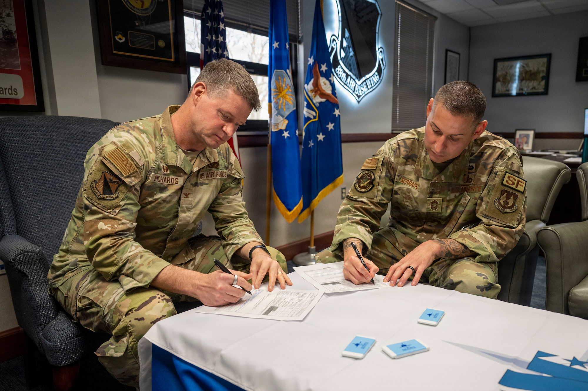 Col Richards and Chief Master Sergeant Serrano sit at a table and each sign their AFAF pledge form.